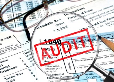 Audit in red with tax forms in background